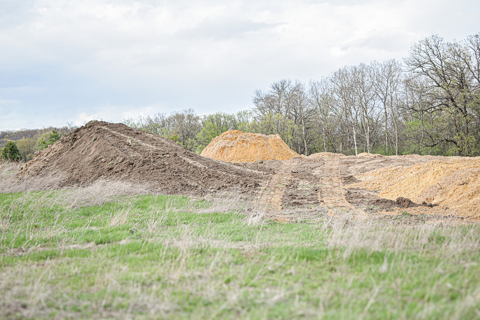 Two-toned subsoil and topsoil mounds staged at the south edge of the cleared pad.