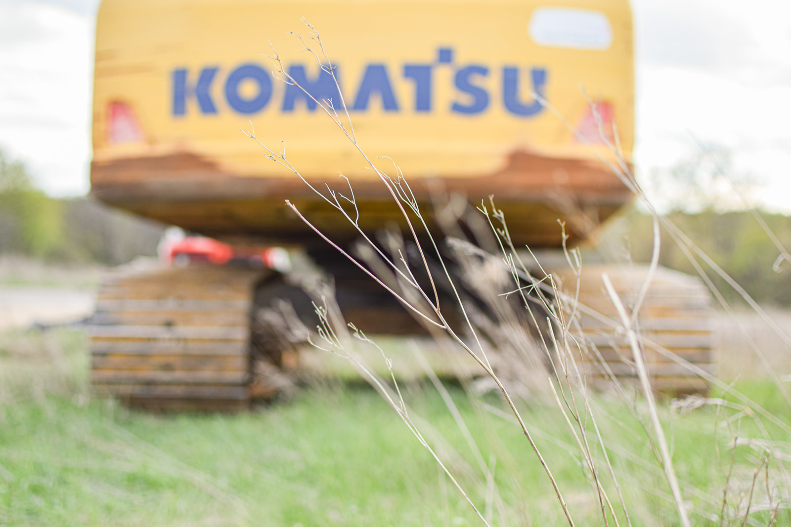 Spring prairie grass in the foreground with an excavator soft-focus on the pad behind.
